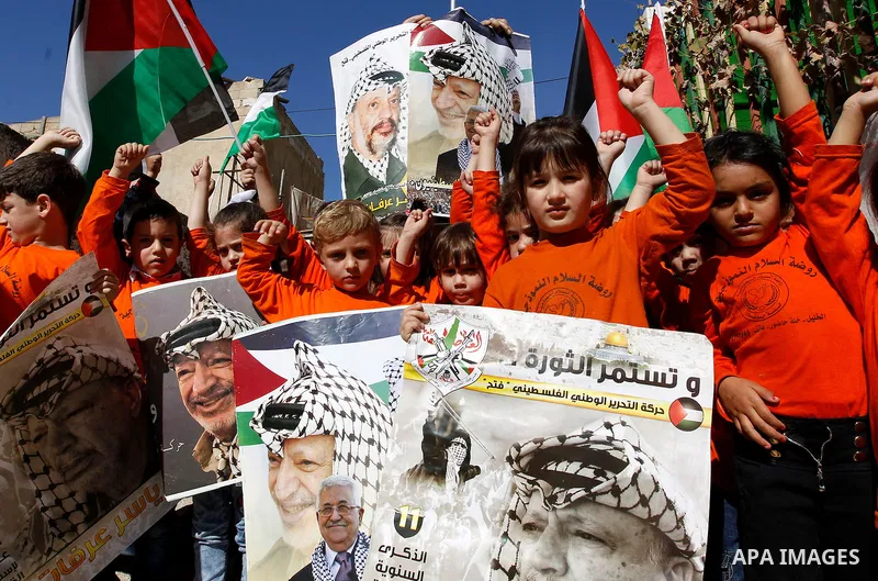 Palestinian children hold posters of the late Palestinian leader Yasser Arafat to mark the 12 anniversary of his death in the West Bank city of Hebron, 10 November 2016. Photo by Wisam Hashlamoun
