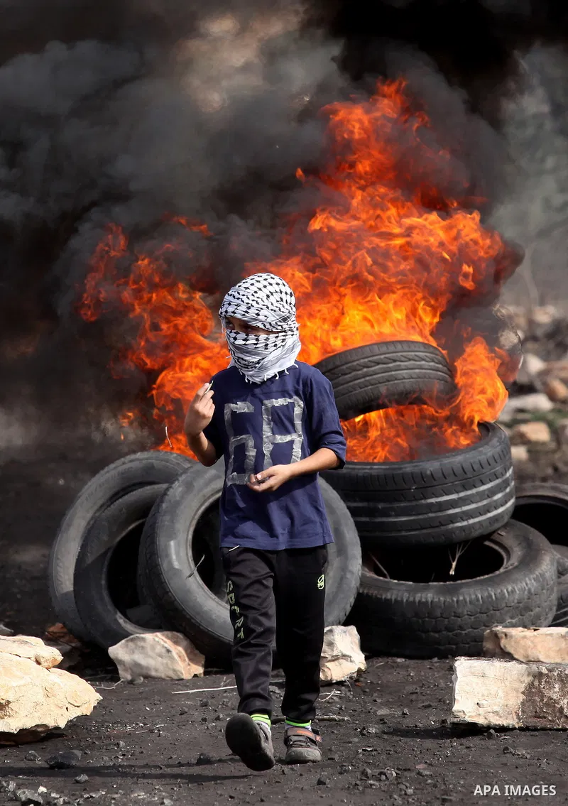 A Palestinian protester stands in front of burning tires during clashes with Israeli security forces following a demonstration against the expropriation of Palestinian land by Israel on November 11, 2016 in the village o...