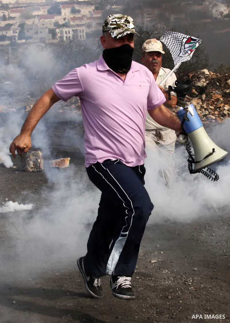 Palestinian protesters run for cover from tear gas canister fired by Israeli security forces during clashes following a demonstration against the expropriation of Palestinian land by Israel on November 11, 2016 in the vi...