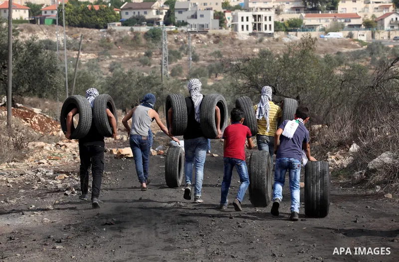 Palestinian protesters carry tires to throw on a fire during clashes with Israeli security forces following a demonstration against the expropriation of Palestinian land by Israel on November 11, 2016 in the village of K...