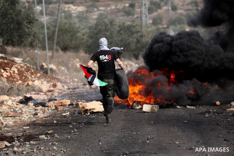 A Palestinian protester throws a tire on a fire during clashes with Israeli security forces following a demonstration against the expropriation of Palestinian land by Israel on November 11, 2016 in the village of Kfar Qa...