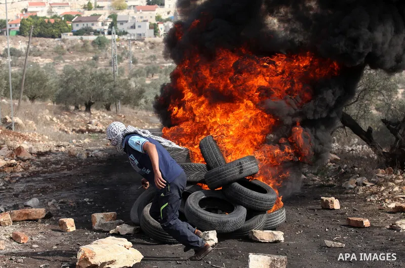 A Palestinian protester throws a tire on a fire during clashes with Israeli security forces following a demonstration against the expropriation of Palestinian land by Israel on November 11, 2016 in the village of Kfar Qa...