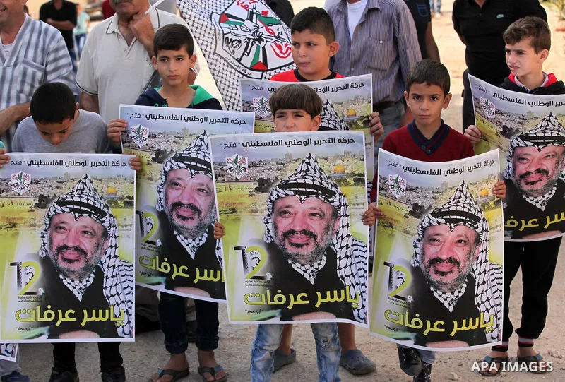 Palestinian protesters wave the national flag and carry posters of Palestinian leader Yasser Arafat, during a demonstration to mark the 12th anniversary of the former leader's death, on November 11, 2016 in the village o...