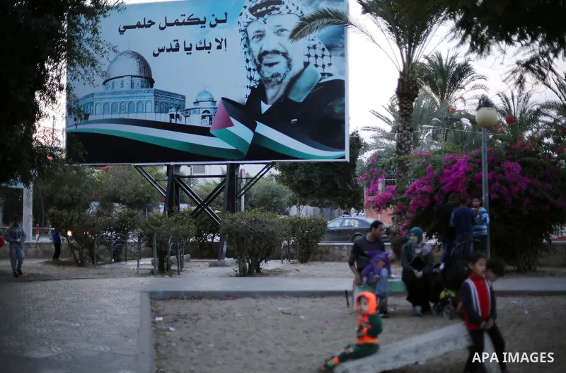 Palestinians walk in front of a poster of the late Palestinian leader Yasser Arafat, on the 12 anniversary of his death in Gaza city on Nov. 11, 2016. Photo by Mohammed Asad