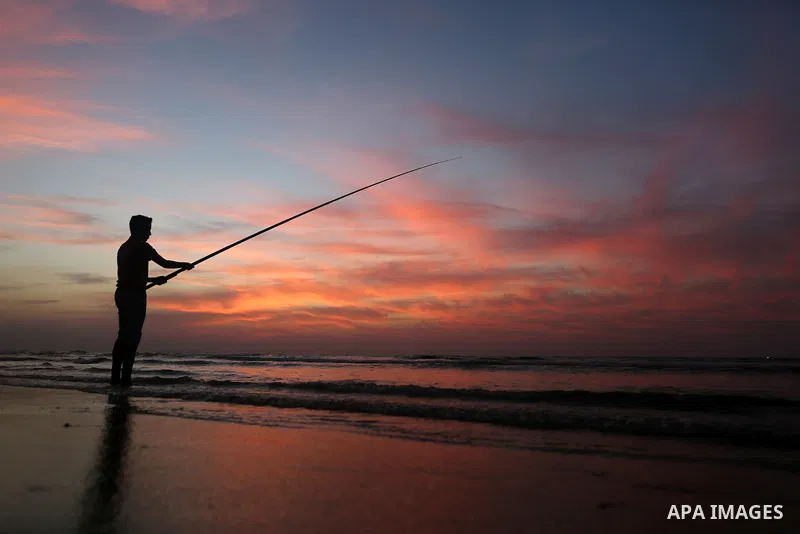 A Palestinian man uses a hook to fishing off the beach of Gaza City on November 14, 2016. Photo by Yasser Qudih