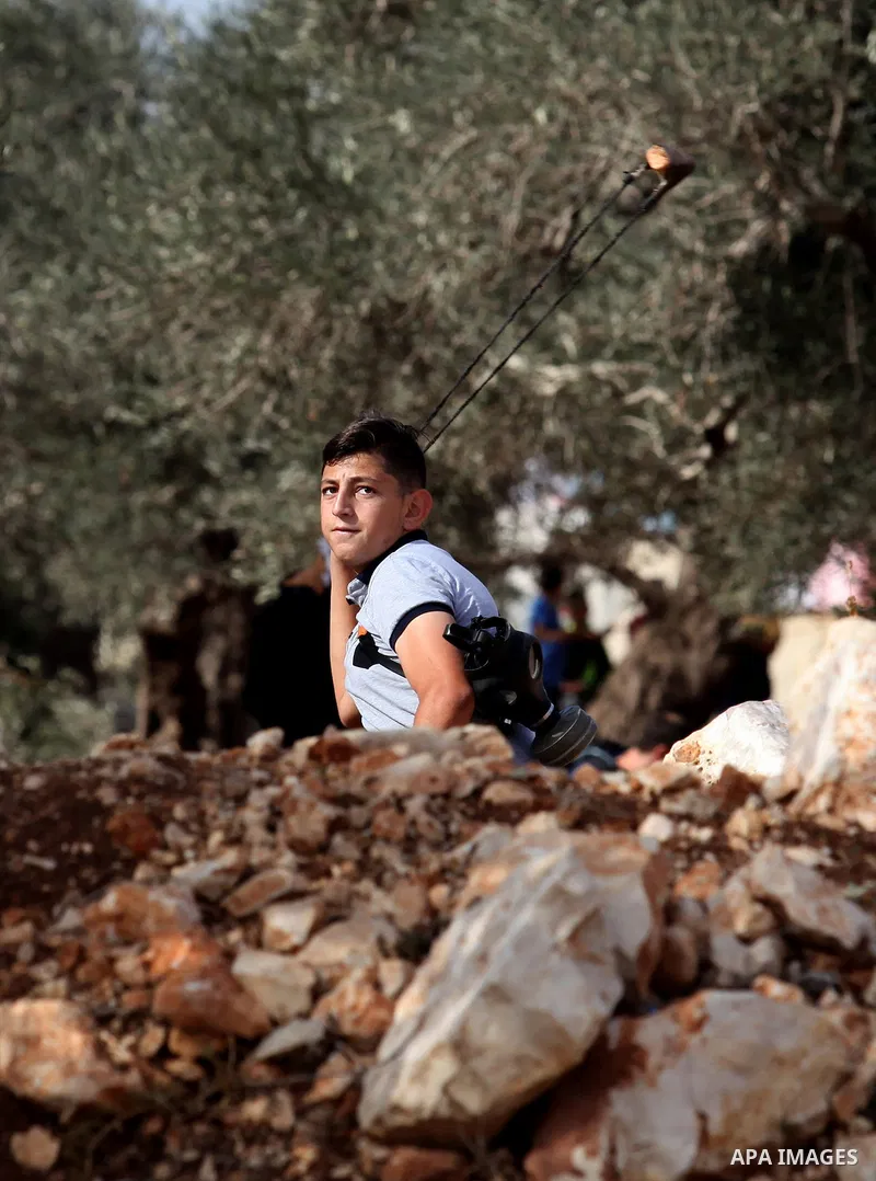 A Palestinian protester uses a slingshot to hurl stones towards Israeli security forces during clashes following a demonstration against the expropriation of Palestinian land by Israel on November 18, 2016 in the village...