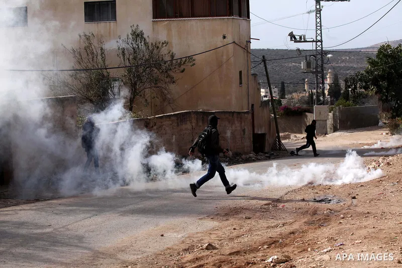 Palestinian protesters run for cover form a tear gas canister fired by Israeli security forces during clashes following a demonstration against the expropriation of Palestinian land by Israel on November 18, 2016 in the...