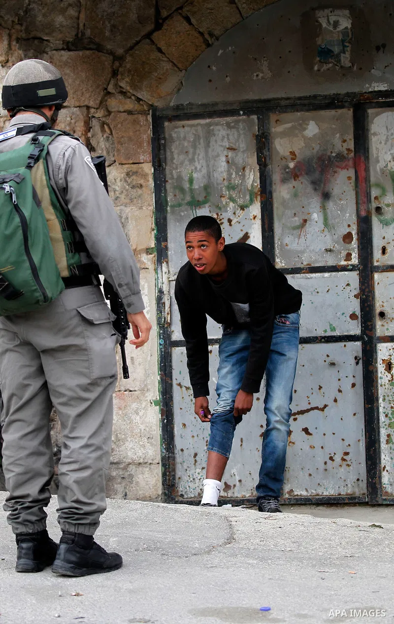 An Israeli soldier checks a Palestinian man at a checkpoint in the West Bank city of Hebron, on Nov. 22, 2016. Photo by Wisam Hashlamoun