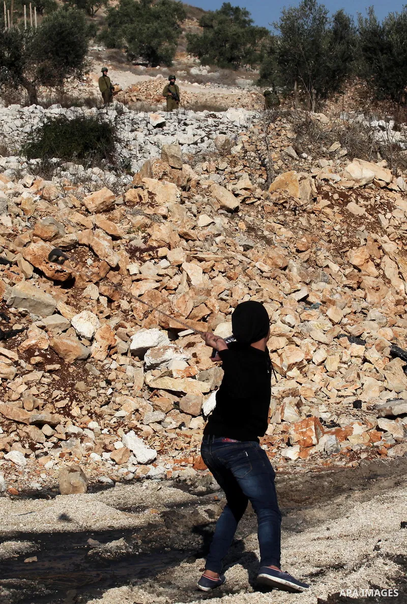 A Palestinian protester uses a slingshot to hurl stones towards Israeli security forces during clashes following a demonstration against the expropriation of Palestinian land by Israel in the village of Kfar Qaddum, near...