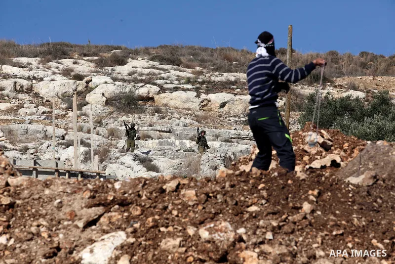 A Palestinian protester uses a slingshot to hurl stones towards Israeli security forces during clashes following a demonstration against the expropriation of Palestinian land by Israel in the village of Kfar Qaddum, near...