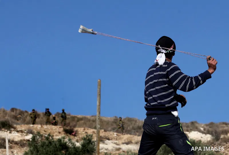 A Palestinian protester uses a slingshot to hurl stones towards Israeli security forces during clashes following a demonstration against the expropriation of Palestinian land by Israel in the village of Kfar Qaddum, near...