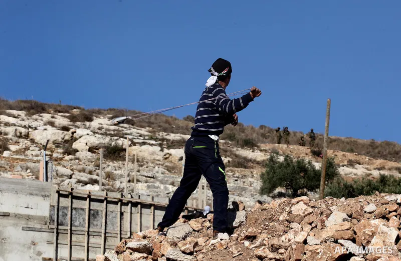 A Palestinian protester uses a slingshot to hurl stones towards Israeli security forces during clashes following a demonstration against the expropriation of Palestinian land by Israel in the village of Kfar Qaddum, near...