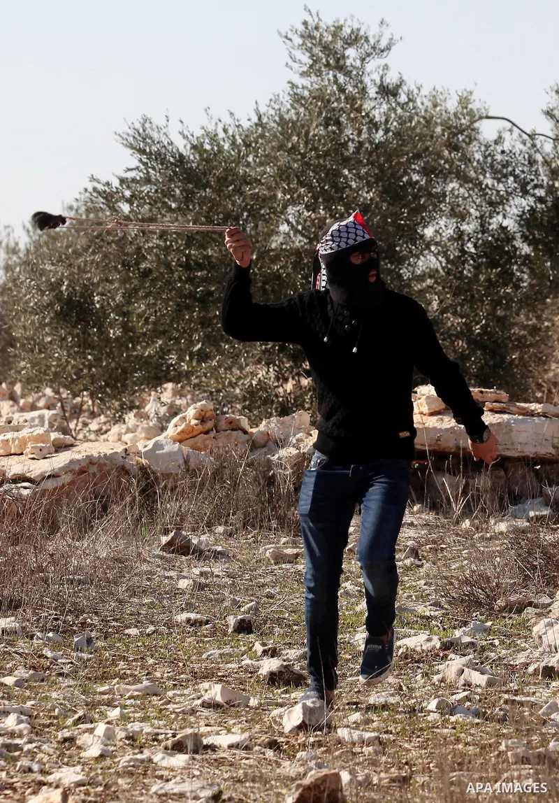 A Palestinian protester uses a slingshot to hurl stones towards Israeli security forces during clashes following a demonstration against the expropriation of Palestinian land by Israel in the village of Kfar Qaddum, near...