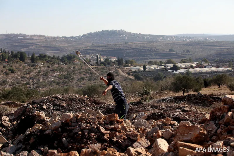 A Palestinian protester uses a slingshot to hurl stones towards Israeli security forces during clashes following a demonstration against the expropriation of Palestinian land by Israel in the village of Kfar Qaddum, near...