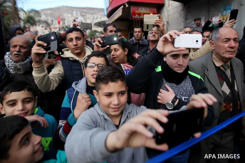 Palestinians take a photo with mobile as Muslim Sufis play musical instruments during a ceremony commemorating the birth of Prophet Mohammed, known in Arabic as "Mawlid al-Nabawi", in the West Bank city of Nablus on Dece...