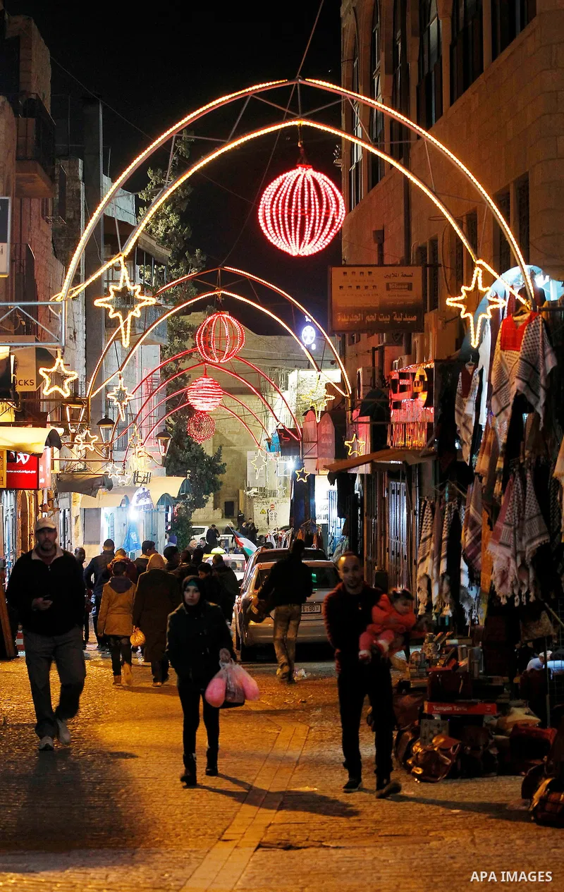 Palestinian Christians walk under lights decorating at the Manger Square near the Church of the Nativity, in the biblical West Bank town of Bethlehem on December 11, 2016. Photo by Wisam Hashlamoun