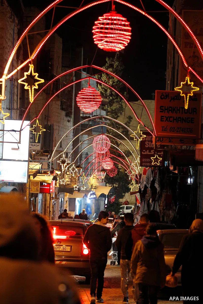 Palestinian Christians walk under lights decorating at the Manger Square near the Church of the Nativity, in the biblical West Bank town of Bethlehem on December 11, 2016. Photo by Wisam Hashlamoun