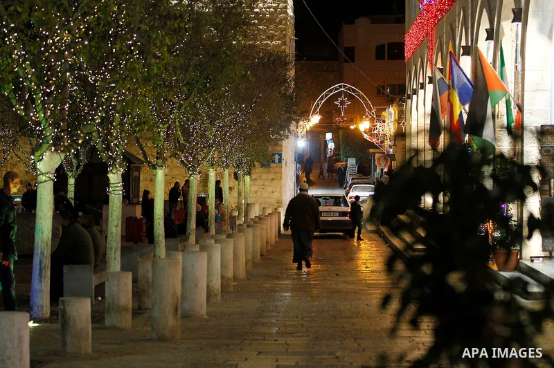 Palestinian Christians walk under lights decorating at the Manger Square near the Church of the Nativity, in the biblical West Bank town of Bethlehem on December 11, 2016. Photo by Wisam Hashlamoun