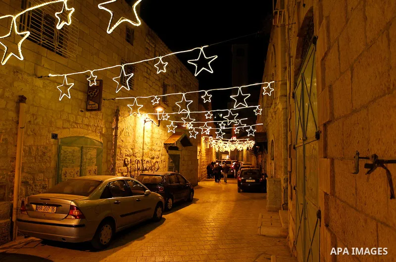 Palestinian Christians walk under lights decorating at the Manger Square near the Church of the Nativity, in the biblical West Bank town of Bethlehem on December 11, 2016. Photo by Wisam Hashlamoun