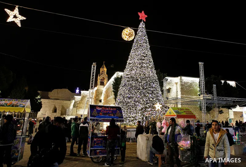 Palestinian Christians walk in front of a Christmas tree at the Manger Square near the Church of the Nativity, in the biblical West Bank town of Bethlehem on December 11, 2016. Photo by Wisam Hashlamoun