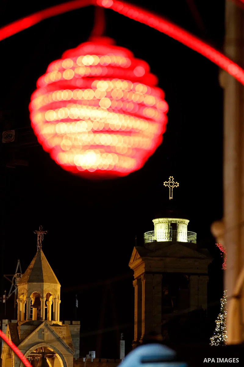 Palestinian Christians walk under lights decorating at the Manger Square near the Church of the Nativity, in the biblical West Bank town of Bethlehem on December 11, 2016. Photo by Wisam Hashlamoun