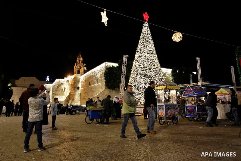 Palestinian Christians walk in front of a Christmas tree at the Manger Square near the Church of the Nativity, in the biblical West Bank town of Bethlehem on December 11, 2016. Photo by Wisam Hashlamoun