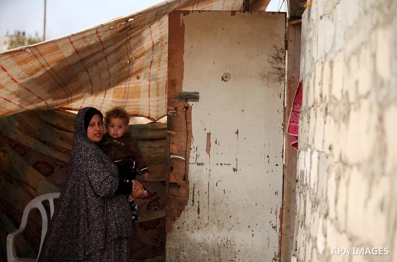 A Palestinian woman holds her child at their dwelling during the winter storm in Khan Younis, in the southern Gaza Strip on December 14, 2016. Photo by Ashraf Amra