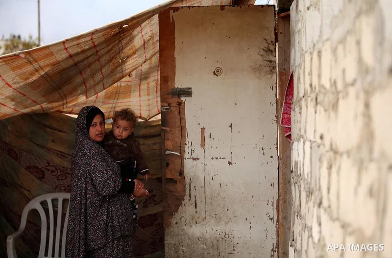 A Palestinian woman holds her child at their dwelling during the winter storm in Khan Younis, in the southern Gaza Strip on December 14, 2016. Photo by Ashraf Amra