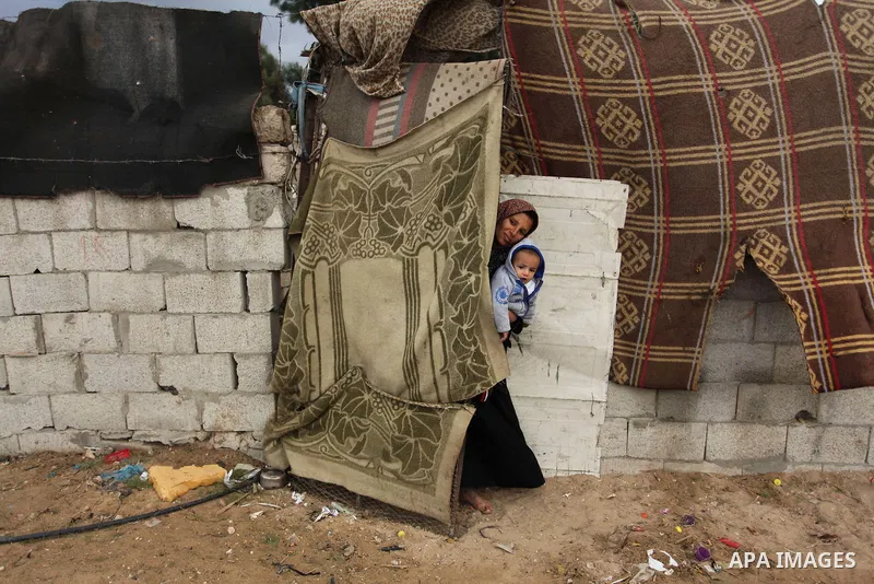 A Palestinian woman holds her child at their dwelling during the winter storm in Khan Younis, in the southern Gaza Strip on December 14, 2016. Photo by Ashraf Amra