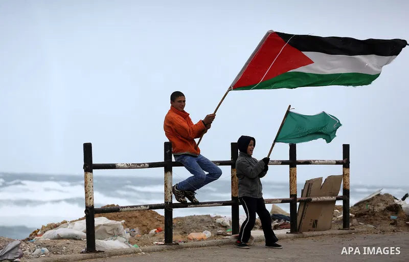 Palestinian children hold flages at a street during a stormy day, in Gaza city on December 14, 2016. Photo by Mohammed Asad