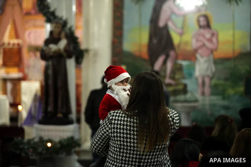 A mother carries her child as English cardinal Vincent Nichols, Archbishop of Westminster, leads a Sunday mass at Der Latin church in Gaza City on December 18, 2016. Photo by Ashraf Amra