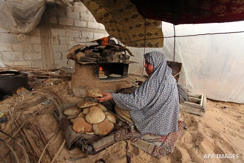 A Palestinian woman bakes bread in a tent outside her dwelling in Khan Younis in the southern Gaza Strip December 19, 2016. Photo by Ashraf Amra