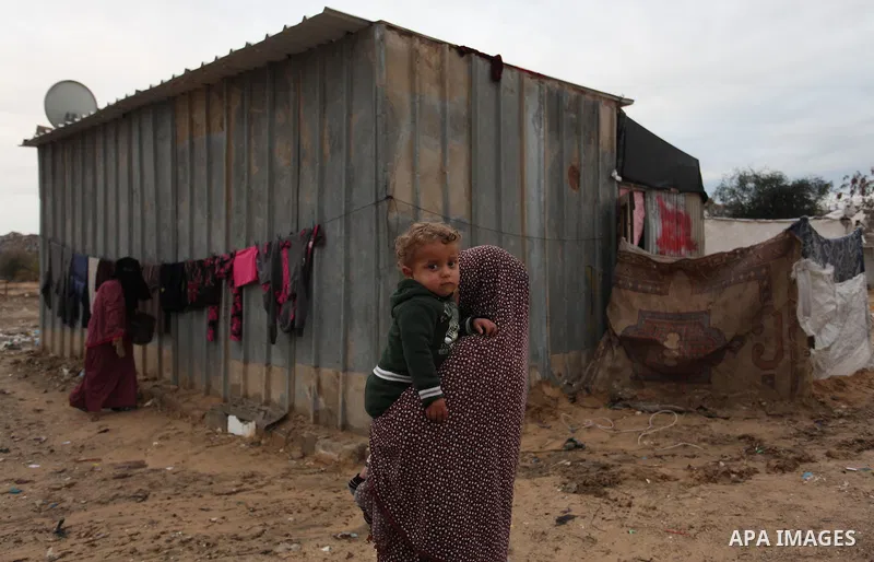 A Palestinian woman carries her son outside her dwelling in Khan Younis in the southern Gaza Strip December 19, 2016. Photo by Ashraf Amra