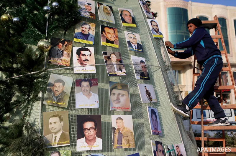 A Palestinian youth uses pictures of Palestinian martyrs to decorate a Christmas tree, in the West Bank town of al-Azariya, east of Jerusalem, on December 22, 2016. Photo by Shadi Hatem