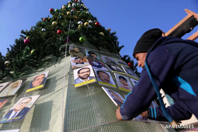 A Palestinian youth uses pictures of Palestinian martyrs to decorate a Christmas tree, in the West Bank town of al-Azariya, east of Jerusalem, on December 22, 2016. Photo by Shadi Hatem