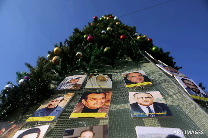 A Palestinian youth uses pictures of Palestinian martyrs to decorate a Christmas tree, in the West Bank town of al-Azariya, east of Jerusalem, on December 22, 2016. Photo by Shadi Hatem