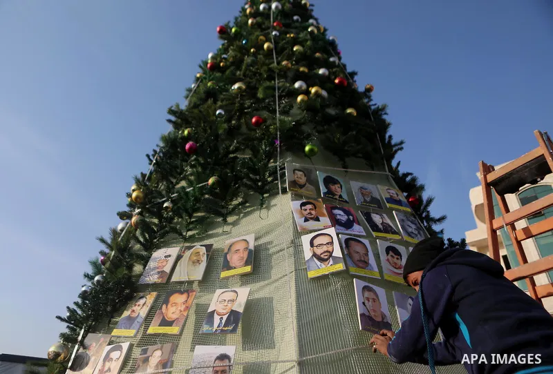 A Palestinian youth uses pictures of Palestinian martyrs to decorate a Christmas tree, in the West Bank town of al-Azariya, east of Jerusalem, on December 22, 2016. Photo by Shadi Hatem