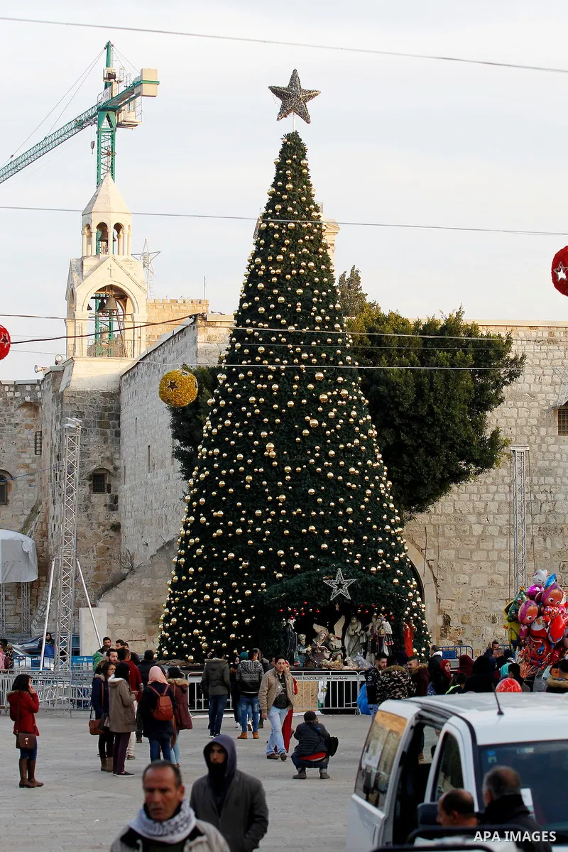 Palestinians walk past a Christmas tree at the Manger Square near the Church of the Nativity, revered as the site of Jesus Christ's birth, on December 22, 2016 in the biblical West Bank town of Bethlehem. Photo by Wisam...