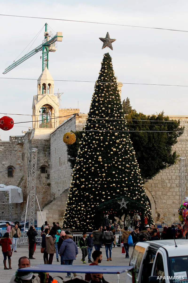 Palestinians walk past a Christmas tree at the Manger Square near the Church of the Nativity, revered as the site of Jesus Christ's birth, on December 22, 2016 in the biblical West Bank town of Bethlehem. Photo by Wisam...