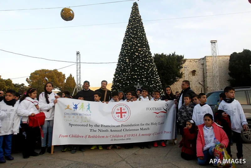Palestinian Christian children take part at the ninth annual Christmas march past a Christmas tree at the Manger Square near the Church of the Nativity, revered as the site of Jesus Christ's birth, on December 22, 2016 i...