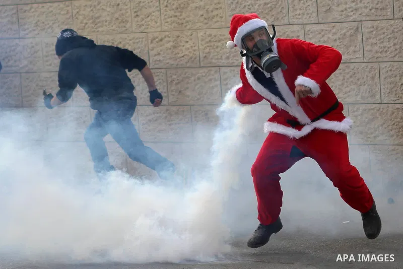 A Palestinian man dressed up as Santa Claus throws back a tear gas grenade fired by Israeli border guard during clashes at a demonstration next to a section of Israel's separation wall in the biblical town of Bethlehem,...
