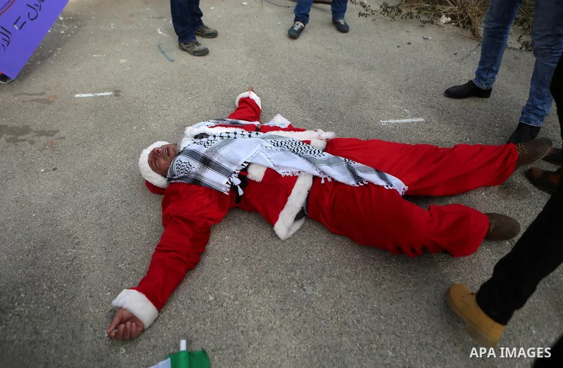 A man tends to a Palestinian protester, dressed as Santa Claus, after inhaling tear gas fired by Israeli border guard during clashes at a demonstration next to a section of Israel's separation wall in the biblical town o...