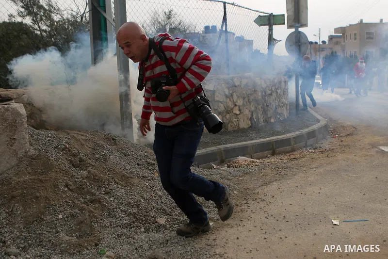 A Palestinian Photographer takes cover form a tear gas grenade fired by Israeli border guard during clashes at a demonstration next to a section of Israel's separation wall in the biblical town of Bethlehem, in the occup...