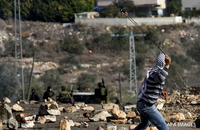 A Palestinian protester uses a slingshot to hurl stones toward Israel security forces during clashes following a demonstration against the expropriation of Palestinian land by Israel in the village of Kfar Qaddum, in the...