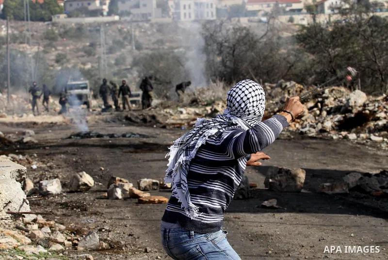 A Palestinian protester uses a slingshot to hurl stones toward Israel security forces during clashes following a demonstration against the expropriation of Palestinian land by Israel in the village of Kfar Qaddum, in the...