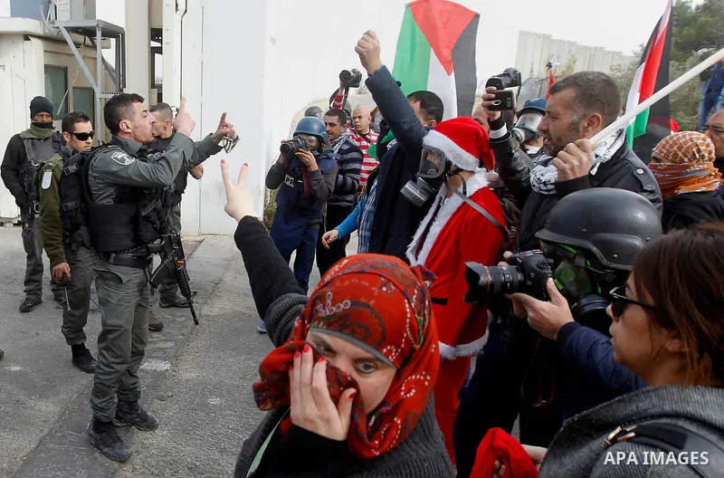 Palestinian protestors, some dressed up as Santa Claus, demonstrate next to a gate at a section of Israel's separation wall in the biblical town of Bethlehem, in the occupied West Bank, on December 23, 2016. Photo by Wis...
