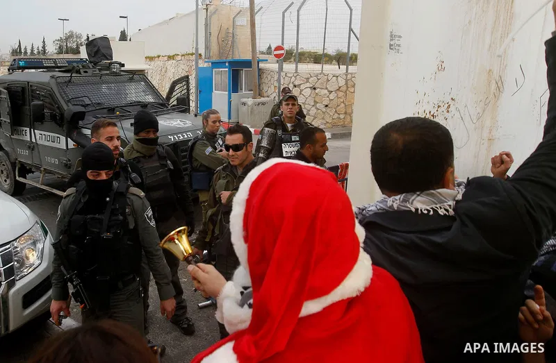Palestinian protestors, some dressed up as Santa Claus, demonstrate next to a gate at a section of Israel's separation wall in the biblical town of Bethlehem, in the occupied West Bank, on December 23, 2016. Photo by Wis...