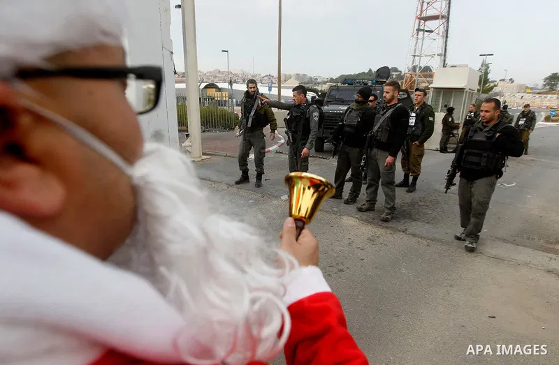 A Palestinian protestor dressed up as Santa Claus, demonstrates next to a gate at a section of Israel's separation wall in the biblical town of Bethlehem, in the occupied West Bank, on December 23, 2016. Photo by Wisam H...