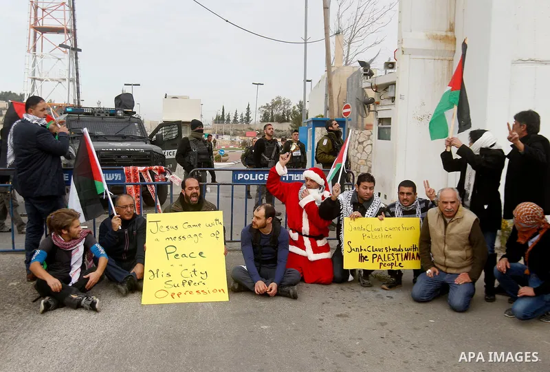Palestinian protestors, some dressed up as Santa Claus, demonstrate next to a gate at a section of Israel's separation wall in the biblical town of Bethlehem, in the occupied West Bank, on December 23, 2016. Photo by Wis...