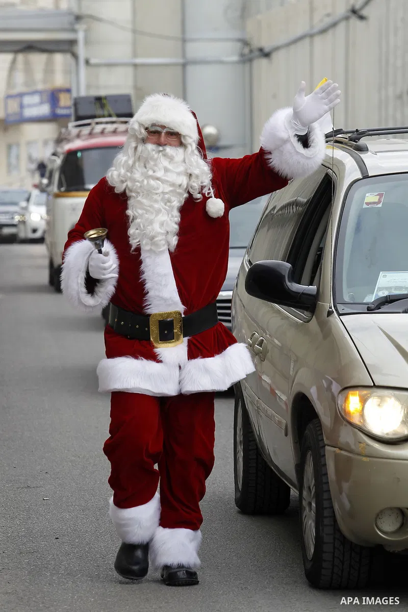 A Palestinian dressed as Santa Claus gestures as the Latin Patriarch of Jerusalem Pierbattista Pizzaballa arrives through an Israeli checkpoint to attend Christmas celebrations, in the city of Bethlehem in the Israeli-oc...